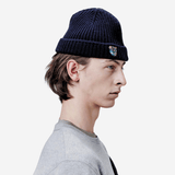 Rickie Beanie Navy - Tonsure. Hold varmen med Tonsure’s strikhue til mænd, der kombinerer tidløst design med maksimal komfort. Fremstillet af blødt og slidstærkt uld, sikrer denne beanie, at du er godt beskyttet mod kulden, samtidig med at du ser stilfuld ud. Den minimalistiske skandinaviske æstetik gør denne hue alsidig og let at kombinere med ethvert outfit.